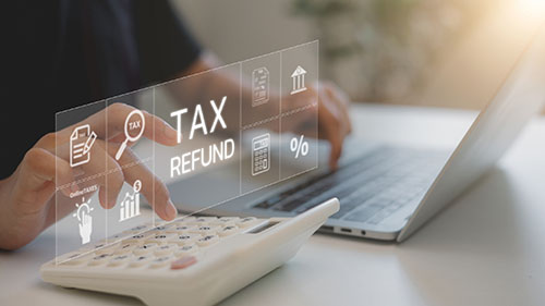 Closeup of a man's hands typing on laptop with calculator nearby and the words "tax refund" overlaid in white text